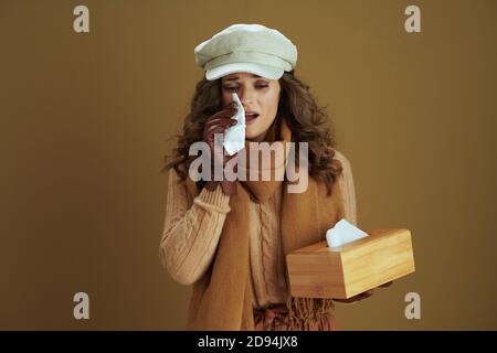Bonjour automne. Élégante femme d'âge moyen en chandail avec mouchoirs en papier et gants en cuir isolés sur beige. Banque D'Images