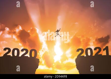 Silhouette de l'homme gras sautant de la colline 2020 à la colline 2021 avec fond de coucher de soleil. Bonne année 2021 Banque D'Images