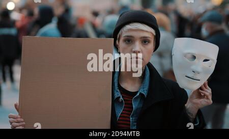 Jeune femme qui retire le masque de théâtre tout en tenant du carton noir dans la foule. Protestation contre la discrimination. Photo de haute qualité Banque D'Images