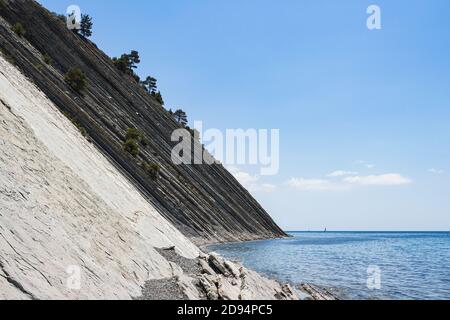 Paysage d'été pittoresque par une journée lumineuse. Plage sauvage en pierre, falaises immenses avec pins et ciel bleu vif avec nuages Banque D'Images