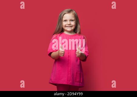 Photo monochrome d'une fille blonde qui fait le geste du signe similaire sur un mur rouge de studio souriant à la caméra Banque D'Images