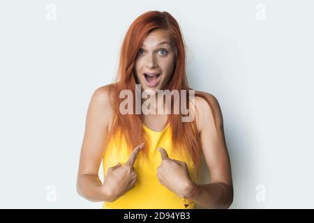 Gingembre la femme caucasienne est stupéfait de se poser dans un t-shirt jaune sur un mur blanc de studio Banque D'Images