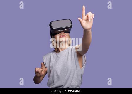 Une femme blonde touche quelque chose en portant un casque de réalité virtuelle un mur de studio violet Banque D'Images
