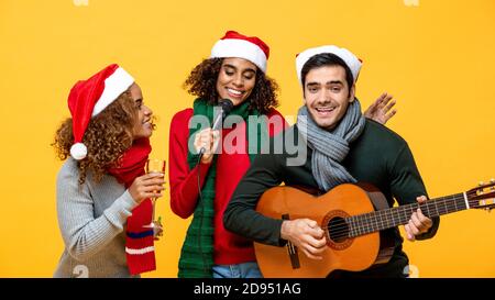 Joyeux amis variés qui chantent et célèbrent Noël fond de studio jaune Banque D'Images