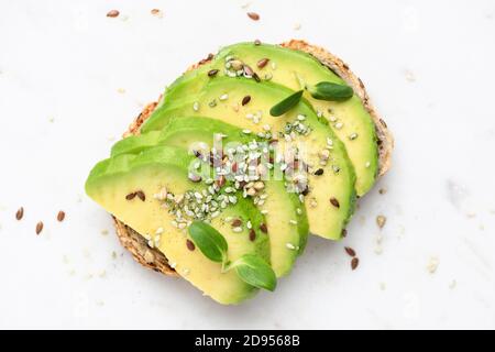 Pain grillé à l'avocat vert végétalien sain avec graines, poudre de spiruline et micro verts isolés sur un fond de marbre, vue du dessus Banque D'Images