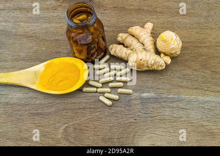 Capsules de plantes de curcuma en bouteille noire, racine de curcuma fraîche et poudre de curcuma dans une cuillère en bois sur fond en bois Banque D'Images