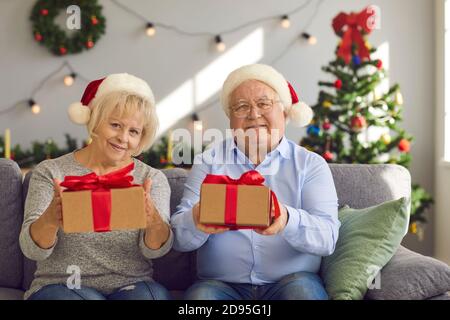Grand-mère et grand-mère heureux en chapeau de père Noël assis sur le canapé Tenue de cadeaux de Noël pour les petits-enfants Banque D'Images