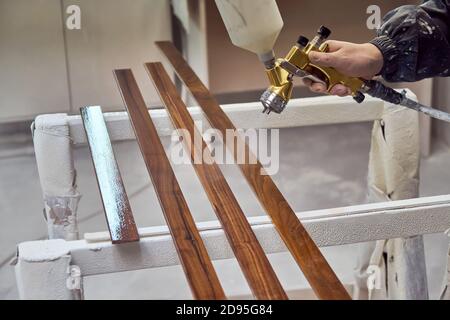 Homme peignant des détails de mobilier dans une cabine de pulvérisation. Travailleur utilisant un pistolet pulvérisateur. Fabrication de meubles. Procédé de fabrication de meubles en bois Banque D'Images