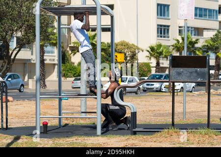 Deux hommes noirs africains, des partenaires de gym, de l'entraînement en plein air ou en plein air sur un appareil de gym faisant biceps tirer ensemble concept santé et fitness Banque D'Images