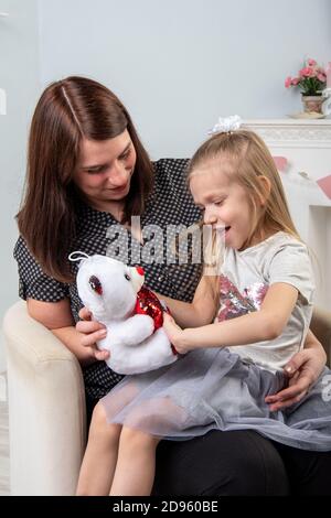 Mère et fille jouant avec un ours en peluche sur fond gris. Traditions familiales. Bonne famille Banque D'Images