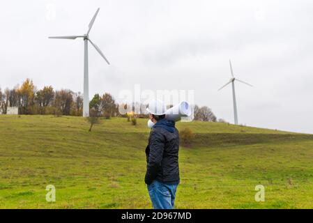 Vue arrière d'un homme portant un casque blanc un plan à l'emplacement de l'éolienne automne ciel nuageux vert pré Banque D'Images