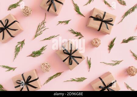 Motif composé de branches de conifères, de boules en rotin, de boîtes-cadeaux en papier kraft sur fond rose pastel Banque D'Images