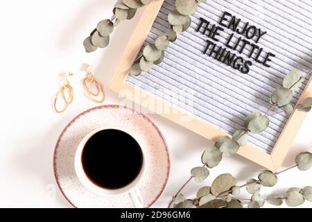 Composition avec des accessoires pour femmes, une tasse de café, des branches d'eucalyptus et un letterboard avec citation appréciez les petites choses Banque D'Images