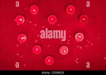 Soirée de Noël ou composition de Saint-Valentin faite de bougies allumées, paillettes sur une surface rouge. Joyeux noël et bonne année 2021, heureux Banque D'Images
