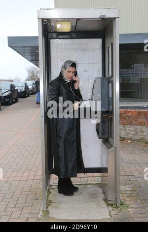 Femme plus âgée, longue blouse noire, qui avait l'air inquiète et préoccupée par la pluie sur le téléphone public. Appeler le service d'urgence, appeler un ami dans une boîte téléphonique sale, un kiosque. Banque D'Images