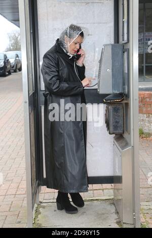 Femme plus âgée, longue blouse noire, qui avait l'air inquiète et préoccupée par la pluie sur le téléphone public. Appeler le service d'urgence, appeler un ami dans une boîte téléphonique sale, un kiosque. Banque D'Images