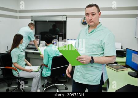 Thème médical .Portrait d'un médecin masculin avec presse-papiers contre un groupe de médecins réunis dans le bureau de l'irm au centre de diagnostic de l'hôpital. Banque D'Images