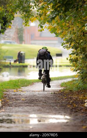 Vue arrière d'un cycliste isolé qui a parcouru son vélo le long du chemin de halage du canal britannique et qui se déplace pour travailler sur une route humide, le matin d'automne de novembre. Banque D'Images