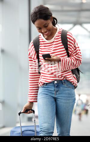 Portrait d'une jeune femme afro-américaine marchant avec une valise et téléphone portable à l'aéroport Banque D'Images