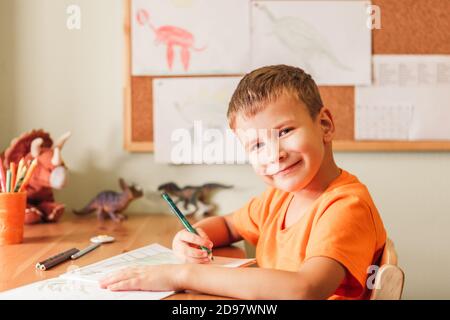 Adorable enfant garçon dessin dinosaures sur la photo avec des crayons de couleur assis près d'un bureau dans sa chambre Banque D'Images