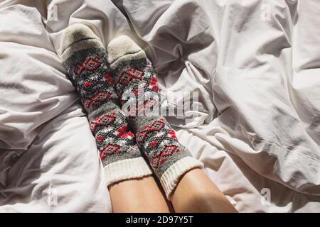 Femme pieds dans des chaussettes en laine confortables sur un lit blanc Banque D'Images