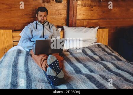 Homme travaillant sur un ordinateur portable assis sur un lit confortable Banque D'Images