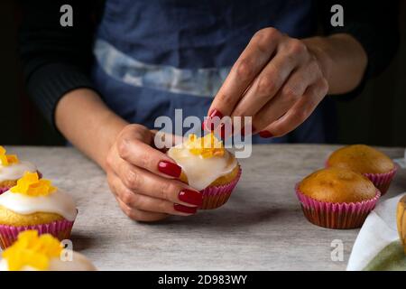 Les mains des femmes de confiserie décorent les muffins aux agrumes. Muffins frais sur une table de confiserie Banque D'Images