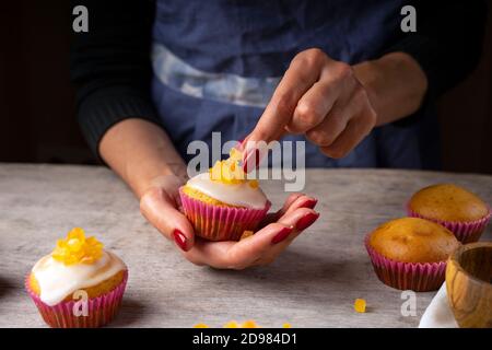 Les mains des femmes de confiserie décorent les muffins aux agrumes. Muffins frais sur une table de confiserie Banque D'Images