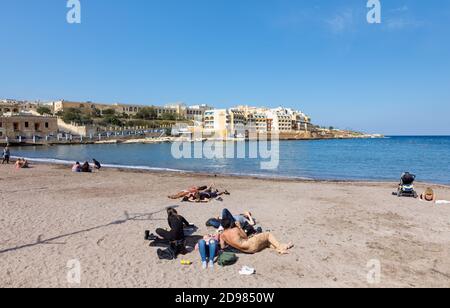 ST. JULIAN - MALTE, 29 mars 2017 : groupe de jeunes se reposer sur la plage de la baie de Saint-Georgeis. Vue sur le Marina Hotel Corinthia BEAC Banque D'Images