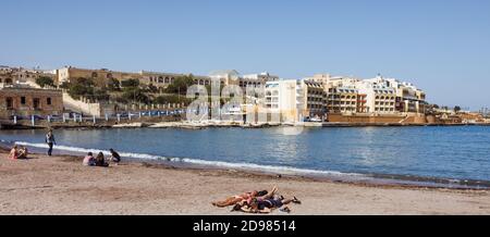 ST. JULIAN - MALTE, 29 mars 2017 : groupe de jeunes se reposer sur la plage de la baie de Saint-Georgeis. Vue sur le Marina Hotel Corinthia BEAC Banque D'Images