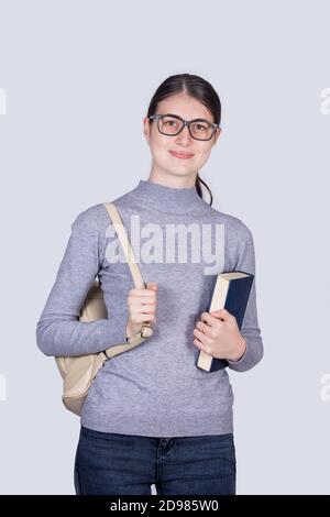 Une jeune fille étudiante confiante tenant un livre et portant son sac à dos. Jeune fille étudiante gaie avec expression positive du visage isolée sur fond blanc. Banque D'Images