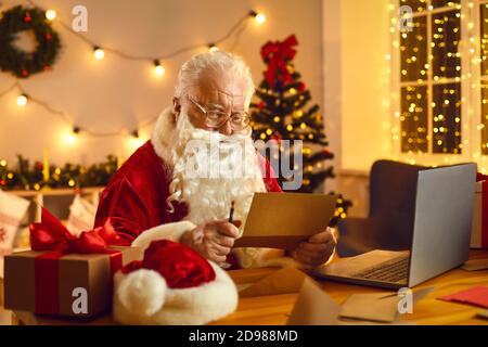 Le Père Noël lit des lettres ou des listes de souhaits d'enfants assis à bureau dans son confortable atelier Banque D'Images