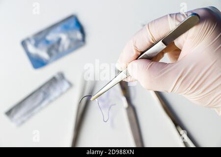 Équipement d'opération chirurgicale, scalpel, couteau, suture et aiguille sur fond blanc. Médecins main tenant la suture. Banque D'Images