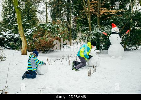 Père avec peu de fils de croisière snowman dans city park Banque D'Images