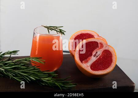 Deux moitiés d'orange rouge, une branche de romarin et un verre de jus d'orange sur une table en bois sur fond clair Banque D'Images