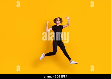 Vue sur toute la longueur de la taille du corps de la jeune fille gaie et mince saut en s'amusant se réjouir isolé couleur jaune vif arrière-plan Banque D'Images