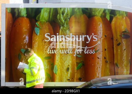 Le chauffeur du camion de livraison de Sainsbury passe devant le minibus qui est garé à l'extérieur d'une propriété pendant la livraison de l'épicerie après une commande en ligne passée par le client. Banque D'Images