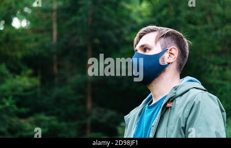 Homme dans le masque de protection noir à l'extérieur. Guy portrait latéral dans le masque médical sur le paysage forestier seul. Protection contre le coronavirus, covid épidémique 19 Banque D'Images