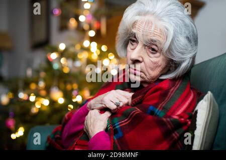Triste et Lonely Senior femme malheureux à propos de passer Noël à Maison seule enveloppée dans une couverture Banque D'Images