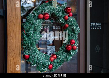 Shanghai, Chine - 10 24 2020: Couronne de Noël traditionnelle de décoration de porte de café faite de branches d'épinette verte et de boules rouges scintillantes. Vacances Banque D'Images