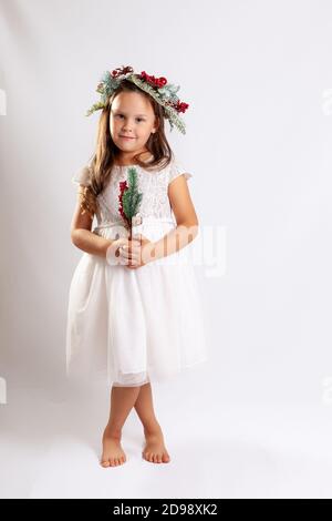 Portrait d'une fille dans une robe blanche princesse et une couronne de Noël, pieds nus, isolée sur un fond bleu Banque D'Images