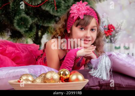 Belle fille en robe de balle se trouve près de l'arbre de Noël sur les oreillers Banque D'Images