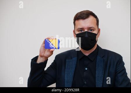 L'homme européen porte un masque classique noir et protège le visage, tient la carte de drapeau de Bosnie-Herzégovine isolée sur fond blanc. Europe coronavirus Covid cou Banque D'Images