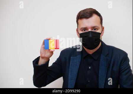 Homme européen porter noir formel et protéger masque, tenir la carte drapeau de Roumanie isolée sur fond blanc. Europe coronavirus Covid pays concept. Banque D'Images