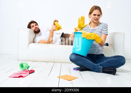 Le mari repose sur le canapé pendant que sa femme nettoie vers le haut de la décoration intérieure Banque D'Images