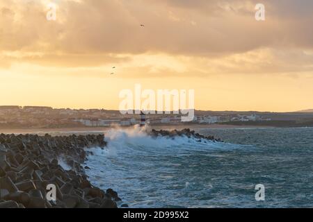 Phare de Peniche avec plage de Supertubos en arrière-plan au coucher du soleil avec des vagues qui s'écrasant, au Portugal Banque D'Images