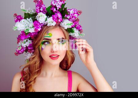 Femme avec fleurs lilas serre-tête sur la tête tenant mascara pinceau appliquant le mascara sur de longues laisses isolées sur le violet clair mur du studio d'arrière-plan Banque D'Images