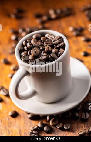 Grains de café rôtis dans une tasse sur une table en bois. Banque D'Images