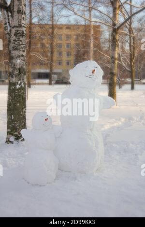 Vue en gros plan de deux bonhommes de neige, grands et petits, avec carottes nez dans un parc urbain d'hiver Banque D'Images