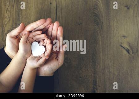 Cœur en papier blanc dans les paumes des enfants et des femmes, vue du dessus. Amour, fête des mères, concept de famille. Banque D'Images